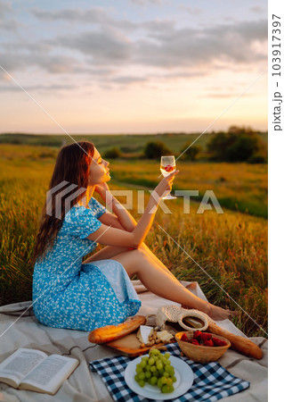Young woman sits on a plaid with a book. Summer picnic in nature. Healthy food. Young woman sits on a plaid with a book. Summer picnic in nature. Healthy food. 103917397