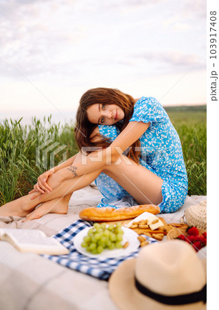Young woman sits on a plaid with a book. Summer picnic in nature. Healthy food. Young woman sits on a plaid with a book. Summer picnic in nature. Healthy food. 103917408