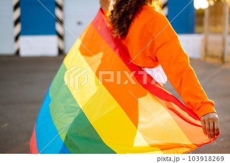 African American lesbian woman with medical face mask posing with lgbt pride flag. Curly woman during quarantine of coronavirus pandemic. African American lesbian woman with medical face mask posing with lgbt pride flag. Curly woman during quarantine of coronavirus pandemic. 103918269