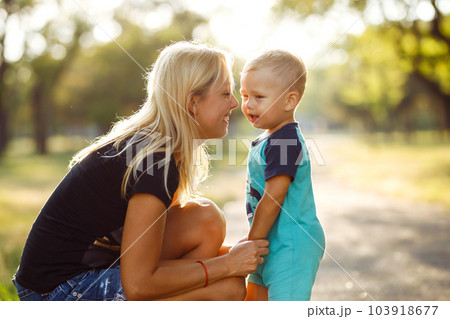 Kiss and hugs of mom and son. Mom and son walk in the summer park. Family holiday and togetherness. Kiss and hugs of mom and son. Mom and son walk in the summer park. Family holiday and togetherness. 103918677