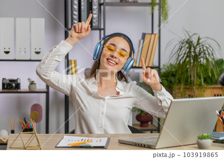 Caucasian businesswoman wearing headphones listening music dancing after working on laptop at office 103919865