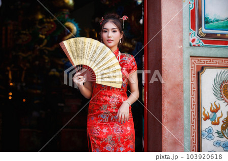 Chinese woman in a red cheongsam dress holding fan at shrine. Concept to celebrate Chinese New Year. 103920618