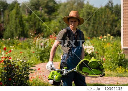 A Young White Man in a Straw Hat is Mowing a Lawn with a Lawn