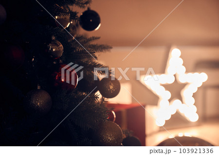 Part of a Christmas tree with balloons on a background with a glowing star. Preparation for the winter holidays, the concept of a New Year's background with space to copy. High quality photo Part of a Christmas tree with balloons on a background with a glowing star. Preparation for the winter holidays, the concept of a New Year's background with space to copy. High quality photo 103921336
