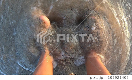 Woman digging feet into wet sand standing near rolling sea waves on sandy beach on summer sunset dawn. Female feet foot toes. Top view. Touching sand. Rest relaxation recreation. Tourist traveler Woman digging feet into wet sand standing near rolling sea waves on sandy beach on summer sunset dawn. Female feet foot toes. Top view. Touching sand. Rest relaxation recreation. Tourist traveler 103921405