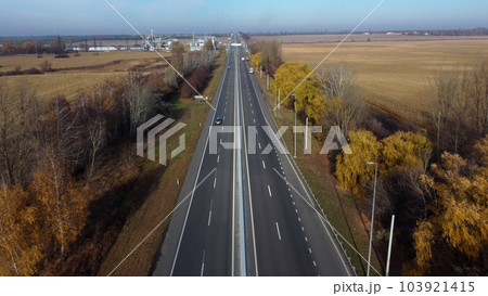Cars driving along the highway on an autumn sunny day. Automobile road with white markings between agricultural fields. View of the cars driving on paved road. automobile vehicles. Aerial drone view.. Cars driving along the highway on an autumn sunny day. Automobile road with white markings between agricultural fields. View of the cars driving on paved road. automobile vehicles. Aerial drone view.. 103921415