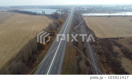 Landscape Highway, driving cars, agricultural fields after harvest, lakes on autumn day. Flying over automobile asphalt road with white markings and many cars. Perspective scenery. Aerial drone view Landscape Highway, driving cars, agricultural fields after harvest, lakes on autumn day. Flying over automobile asphalt road with white markings and many cars. Perspective scenery. Aerial drone view 103921417