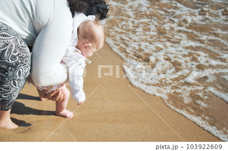 Barefoot mother and baby daughter on the sea shore on a sandy beach walking close to the surf foam on the waves Barefoot mother and baby daughter on the sea shore on a sandy beach walking close to the surf foam on the waves 103922609