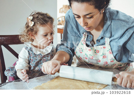 Mother and daughter baking cookies in the kitchen - flattening pastry dough with a rolling pin Mother and daughter baking cookies in the kitchen - flattening pastry dough with a rolling pin 103922618