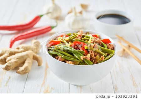 Chinese fried string beans with pork and soy sauce on a wooden table with ingredients, garlic, hot pepper, ginger. 103923391