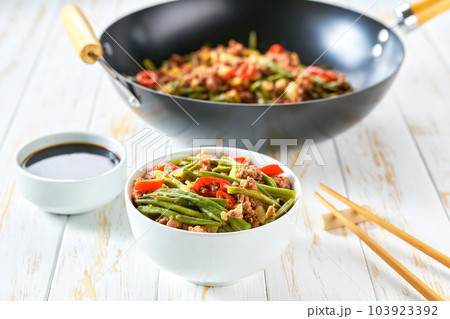 chinese cuisine sichuan stir-fried green beans in a wok with pork, garlic, hot pepper, ginger on a wooden table. 103923392