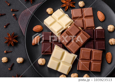 A mix of several types of delicious sweet chocolate broken into cubes on a black plate A mix of several types of delicious sweet chocolate broken into cubes on a black plate 103923513