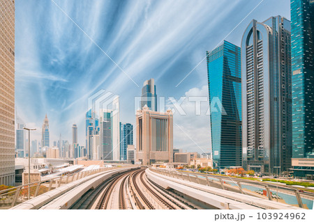 Metro road among glass skyscrapers in Dubai. Metropolitan railway among modern glass skyscrapers in Dubai. Traffic on street in Dubai. Urban background 103924962