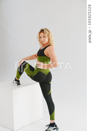a blonde in a tracksuit makes stretching lunges on a white cube 103925228
