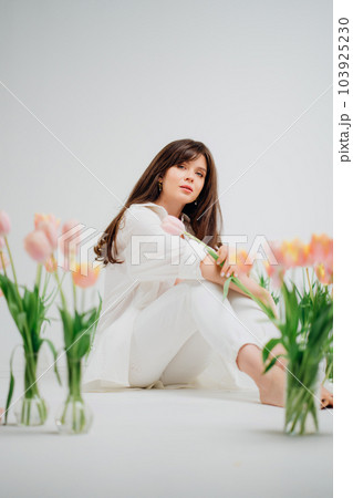 gentle brunette in white sits on the floor with vases of tulips gentle brunette in white sits on the floor with vases of tulips 103925230