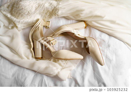 The bride's shoes and wedding dress on the bed. The bride's shoes and wedding dress on the bed. 103925232