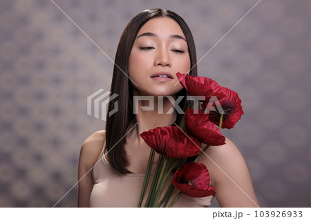 Young attractive asian woman holding poppy bunch, looking at red flower. Beautiful fashion model posing with bright summer blossoms branch, standing with blooming plants bouquet Young attractive asian woman holding poppy bunch, looking at red flower. Beautiful fashion model posing with bright summer blossoms branch, standing with blooming plants bouquet 103926933