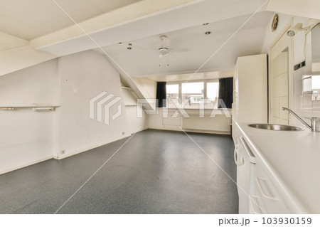an empty room with white walls and black flooring on the right, there is a large window to the left an empty room with white walls and black flooring on the right, there is a large window to the left 103930159