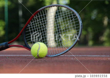 Tennis racquet and yellow tennis ball on outdoor court 103931558