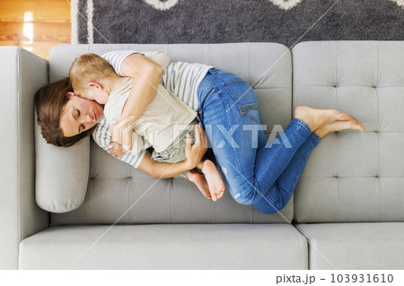 Mother embraces her cute little son while laying together on the couch Mother embraces her cute little son while laying together on the couch 103931610