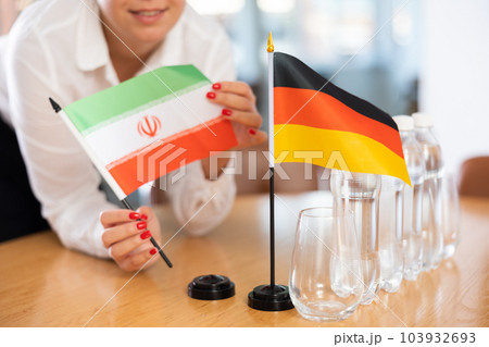 Little flag of Germany on table and flag of Iran put next to it by young woman Little flag of Germany on table and flag of Iran put next to it by young woman 103932693