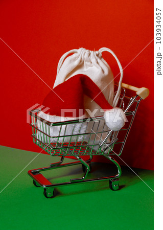 Santa hat in shopping trolley on isometric red green background. Online shopping holiday concept Copy space for your text. Mock up for advertisement. Holiday Christmas composition. Minimalistic Santa hat in shopping trolley on isometric red green background. Online shopping holiday concept Copy space for your text. Mock up for advertisement. Holiday Christmas composition. Minimalistic 103934057