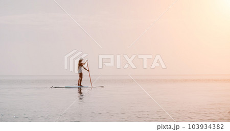 Woman sea sup. Close up portrait of happy young caucasian woman with long hair looking at camera and smiling. Cute woman portrait in bikini posing on sup board in the sea Woman sea sup. Close up portrait of happy young caucasian woman with long hair looking at camera and smiling. Cute woman portrait in bikini posing on sup board in the sea 103934382