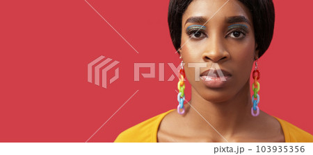 Lgbt portrait. Diversity colors. Equality right. Confident proud woman face bright makeup rainbow earrings on pink empty space background. 103935356