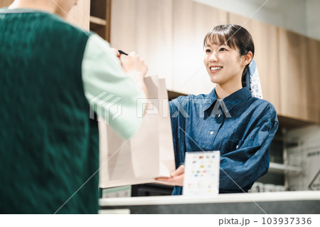 買い物客に紙袋を渡す女性店員 103937336