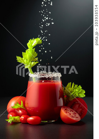 Sea salt is poured into a glass of tomato juice with celery. 103938554