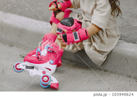 Child in a summer park. Kid in a pink helmet. Little girl with a roller. Child in a summer park. Kid in a pink helmet. Little girl with a roller. 103940624