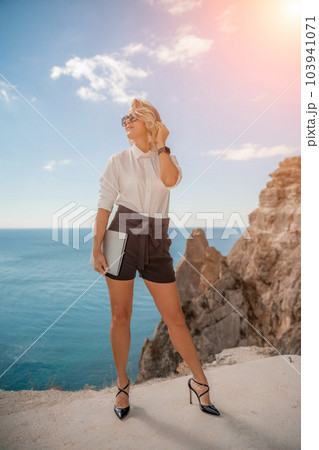 Freelance women sea working on a computer. Pretty middle aged woman with computer and phone outdoors with beautiful sea view. The concept of remote work. Freelance women sea working on a computer. Pretty middle aged woman with computer and phone outdoors with beautiful sea view. The concept of remote work. 103941071
