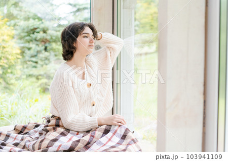 Portrait caucasian young woman sitting near window apartments in a white sweater Portrait caucasian young woman sitting near window apartments in a white sweater 103941109