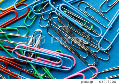 Close up of stack of multi coloured paper clips on blue background Close up of stack of multi coloured paper clips on blue background 103941208