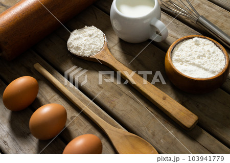 High angle view of flour with milk, sugar, eggs, wooden spoons, rolling pin and whisk on table High angle view of flour with milk, sugar, eggs, wooden spoons, rolling pin and whisk on table 103941779