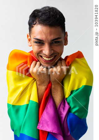Portrait of happy biracial transgender man holding rainbow flag on white background Portrait of happy biracial transgender man holding rainbow flag on white background 103941820