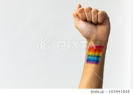 Close up of hand of biracial man clenching fist with rainbow flag on white background, copy space 103941848