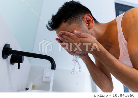Biracial transgender man washing face in bathroom 103941960