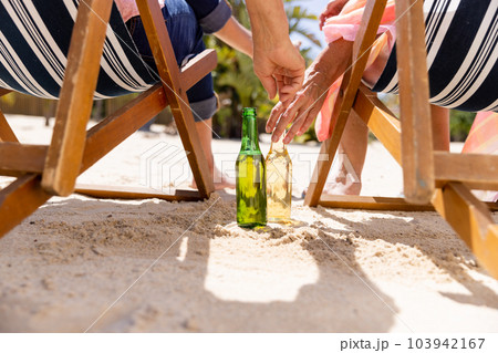 Low section of caucasian senior couple with beer bottles sitting on deck chairs at beach 103942167