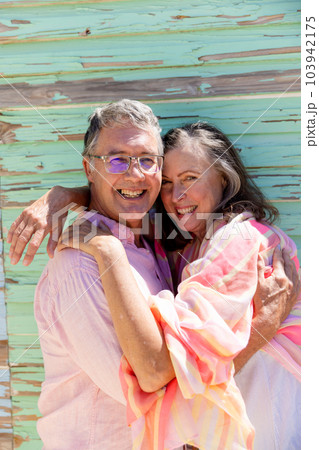 Portrait of smiling caucasian senior couple embracing and standing against wooden wall 103942175