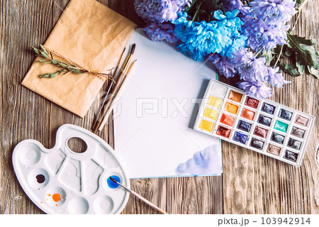 Palette of watercolor paints, brushes and paper for a water color on wooden background, close up. Flat lay, spring background with copy space 103942914