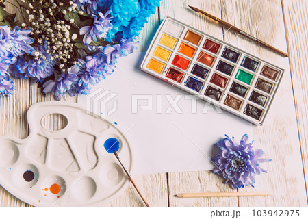 Palette of watercolor paints, brushes and paper for a water color on wooden background, close up. Flat lay, spring background with copy space Palette of watercolor paints, brushes and paper for a water color on wooden background, close up. Flat lay, spring background with copy space 103942975
