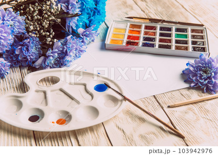 Palette of watercolor paints, brushes and paper for a water color on wooden background, close up. Flat lay, spring background with copy space Palette of watercolor paints, brushes and paper for a water color on wooden background, close up. Flat lay, spring background with copy space 103942976