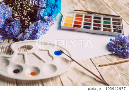 Palette of watercolor paints, brushes and paper for a water color on wooden background, close up. Flat lay, spring background with copy space Palette of watercolor paints, brushes and paper for a water color on wooden background, close up. Flat lay, spring background with copy space 103942977