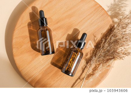 Amber glass bottle on beige background. Wooden podium. Natural skin care SPA beauty product design. Mineral organic oil cosmetics. Minimal Flat lay Amber glass bottle on beige background. Wooden podium. Natural skin care SPA beauty product design. Mineral organic oil cosmetics. Minimal Flat lay 103943606
