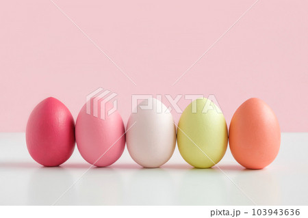 Easter banner with colorful Easter Egg in a row on white table and pink background. Above view with copy space. Easter decorated eggs frame. Easter banner with colorful Easter Egg in a row on white table and pink background. Above view with copy space. Easter decorated eggs frame. 103943636