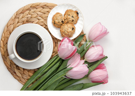 White cup of coffee with pink tulips on white background. Morning coffee on wicker tray. View from above of morning coffee, cookies and flowers. Flat lay. Breakfast in bed Stylish home interior decor White cup of coffee with pink tulips on white background. Morning coffee on wicker tray. View from above of morning coffee, cookies and flowers. Flat lay. Breakfast in bed Stylish home interior decor 103943637
