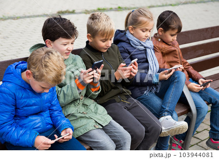 Kids playing with smartphones on bench 103944081