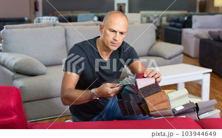 Portrait of man holding and choosing samples of upholstery fabric in furniture salon 103944649