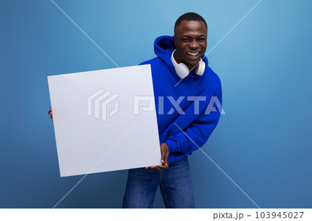 handsome young african man showing a white board with a mockup for advertising on the background handsome young african man showing a white board with a mockup for advertising on the background 103945027